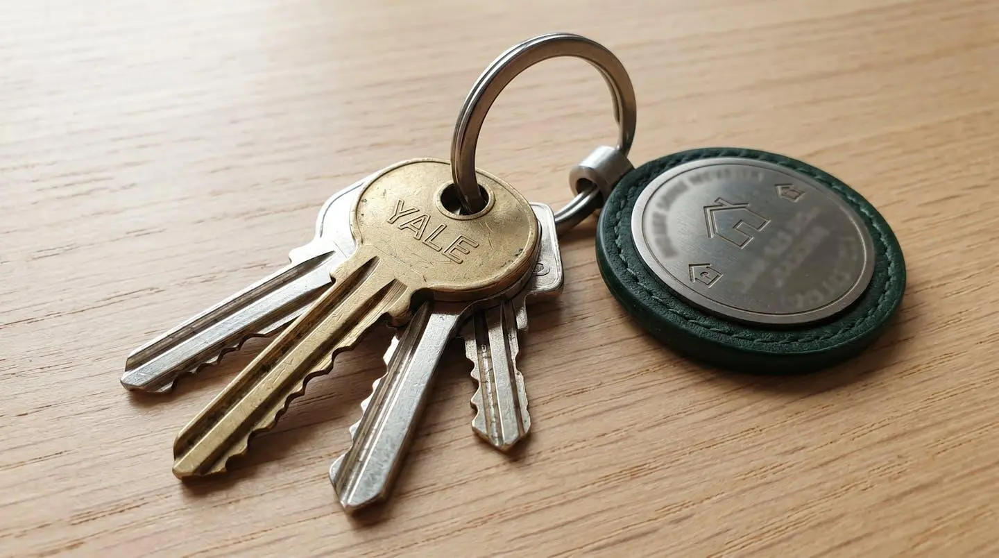 Un trousseau de clés de maison posé sur une surface en bois clair, avec un porte-clés élégant, photographié en macro avec une lumière latérale douce
